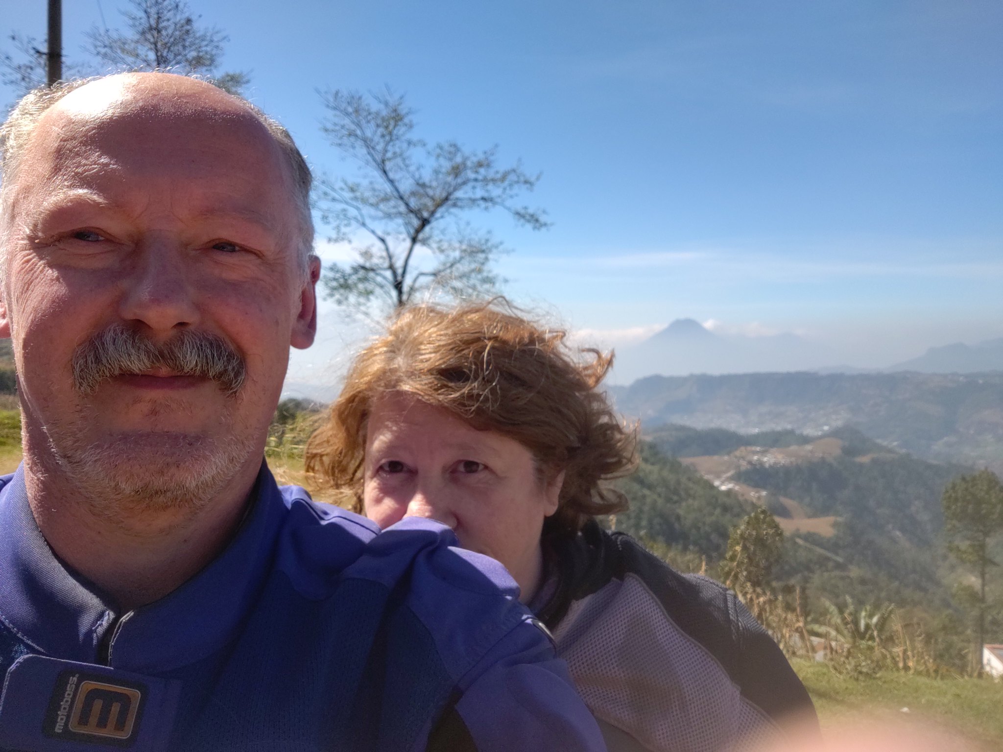 two people looking at the camera with a beautiful landscape
        behind them