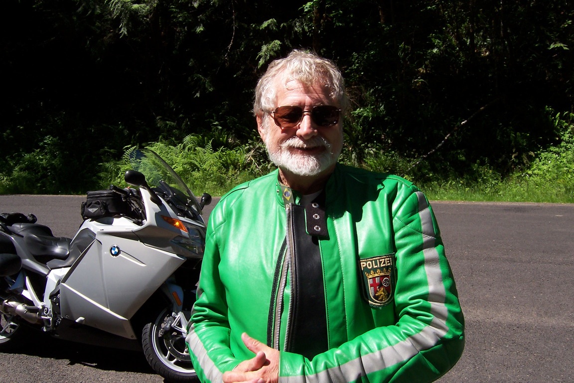 Eric Haws, wearing his German police leather jacket, standing in front of his motorcycle.