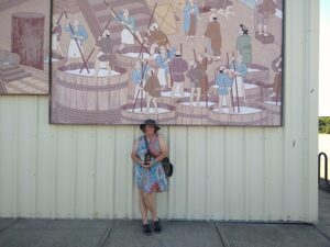 A woman poses below a very large mural depicting the ancient way sake was made in Japan