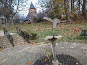 in the background is the castle-like museum of the park. In the foreground is a sculpture of a humming bird drinking from a flower. 