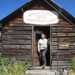 A woman stands in the doorway of an old cabin.