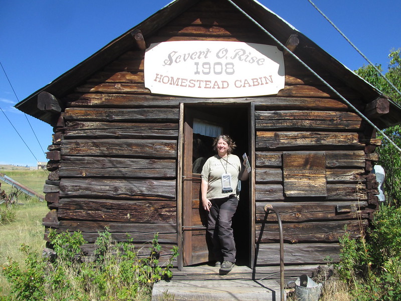 A woman stands in the doorway of an old cabin.