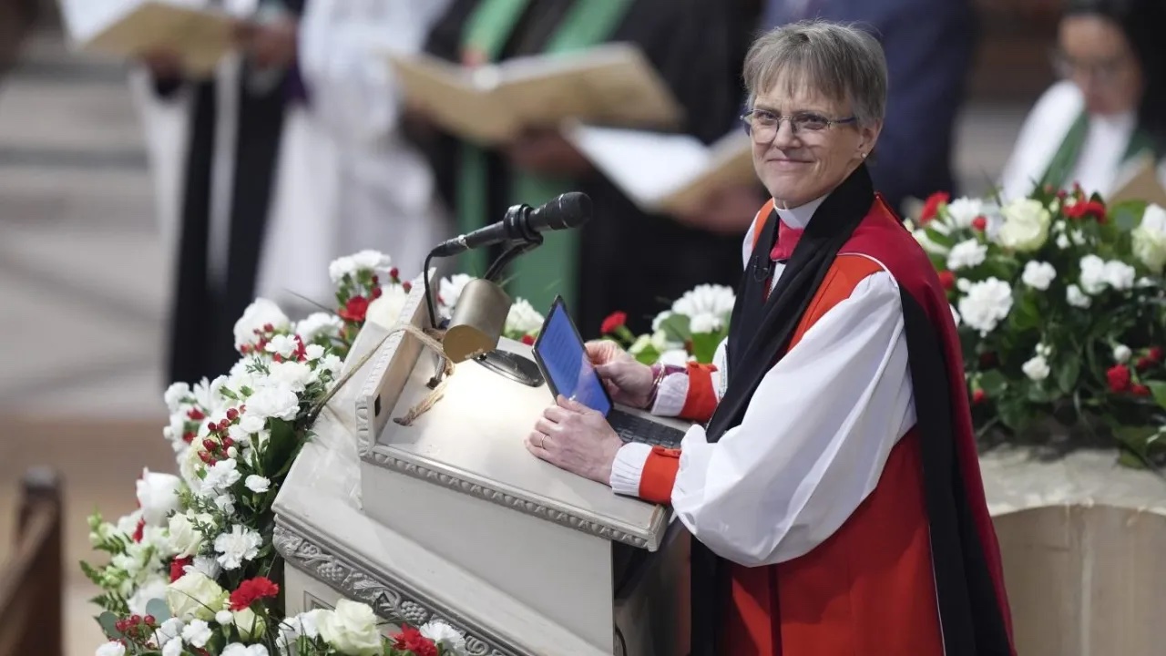 A smiling Bishop stands at the church lectern, which is covered in flowers.