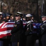 Members of different US military branches carry a coffin draped in the USA flag. It is the coffin of Jimmy Carter.