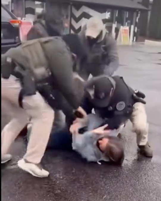 A woman is laying on the ground where she was thrown by the masked men surrounding her.
