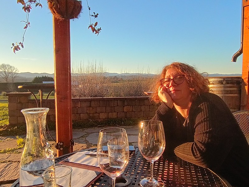A woman sits on an outdoor patio, illuminated by a sunset.