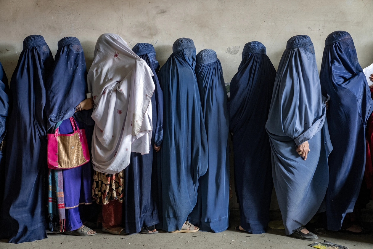 A line of women, all but one in a blue burqa, stand in line.