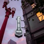The outside of a building, shot from an angle to make it look like a noir film. The neon sign for The Society Hotel is lit against the sky.