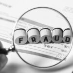A magnifying glass on a document magnifies the word FRAUD on an otherwise blurry document.
