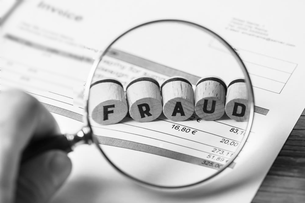 A magnifying glass on a document magnifies the word FRAUD on an otherwise blurry document.