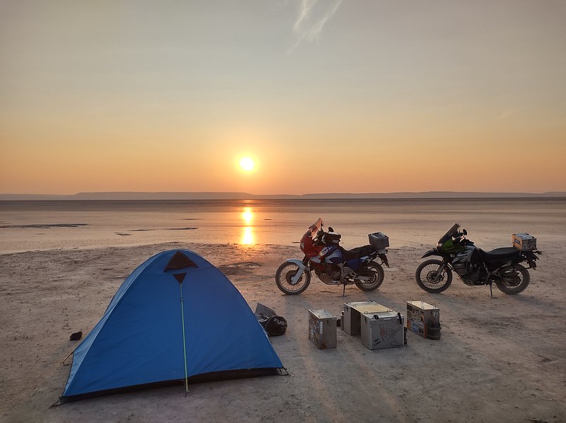 The sun rises over the Alford desert behind two motorcycles, panniers as tables and chairs and a tent.