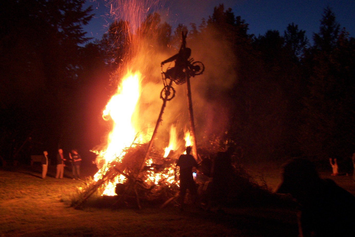 a bonfire
        rages in the night, with the outline of a motorcycle hanging at
        the top in the flames