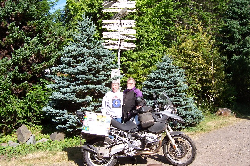 two people stand behind a motorcycle
        and in front of a pole with the names of people who have visited
        them