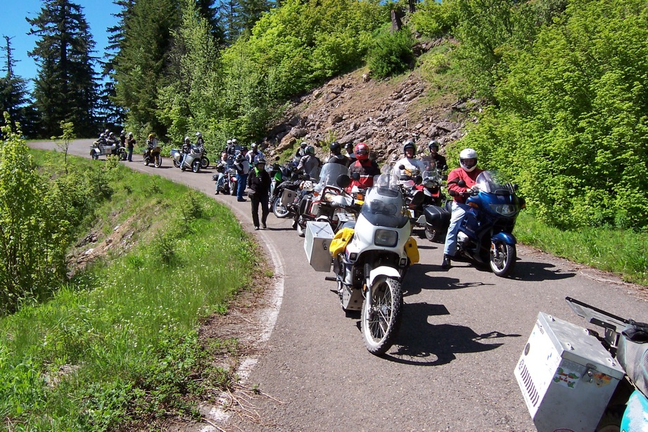 a long line of
        motorcycle riders have stopped on a narrow road in a forrest